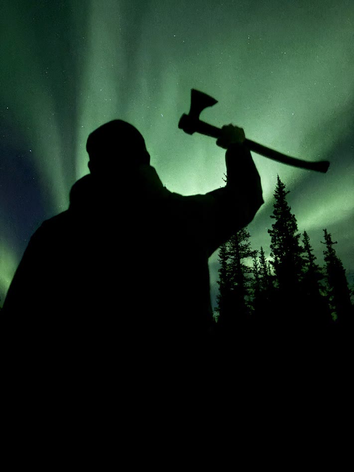 Silhouette raising a Taiga axe under the northern lights