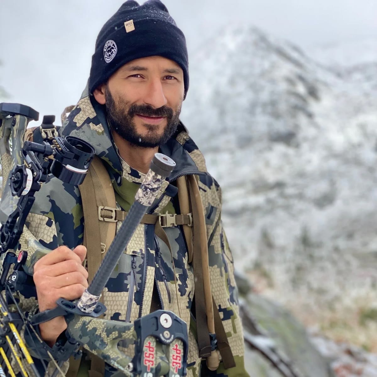 Jordan Jonas smiling with his bow in snowy mountains