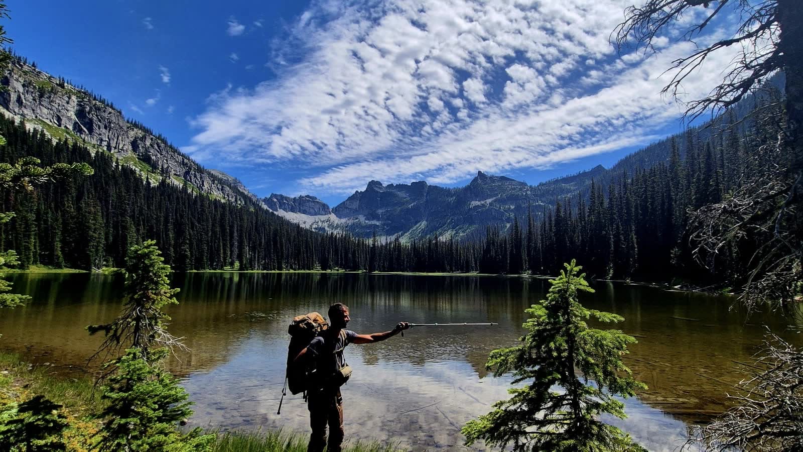 A hiker at the edge of an alpine lake under a big sky