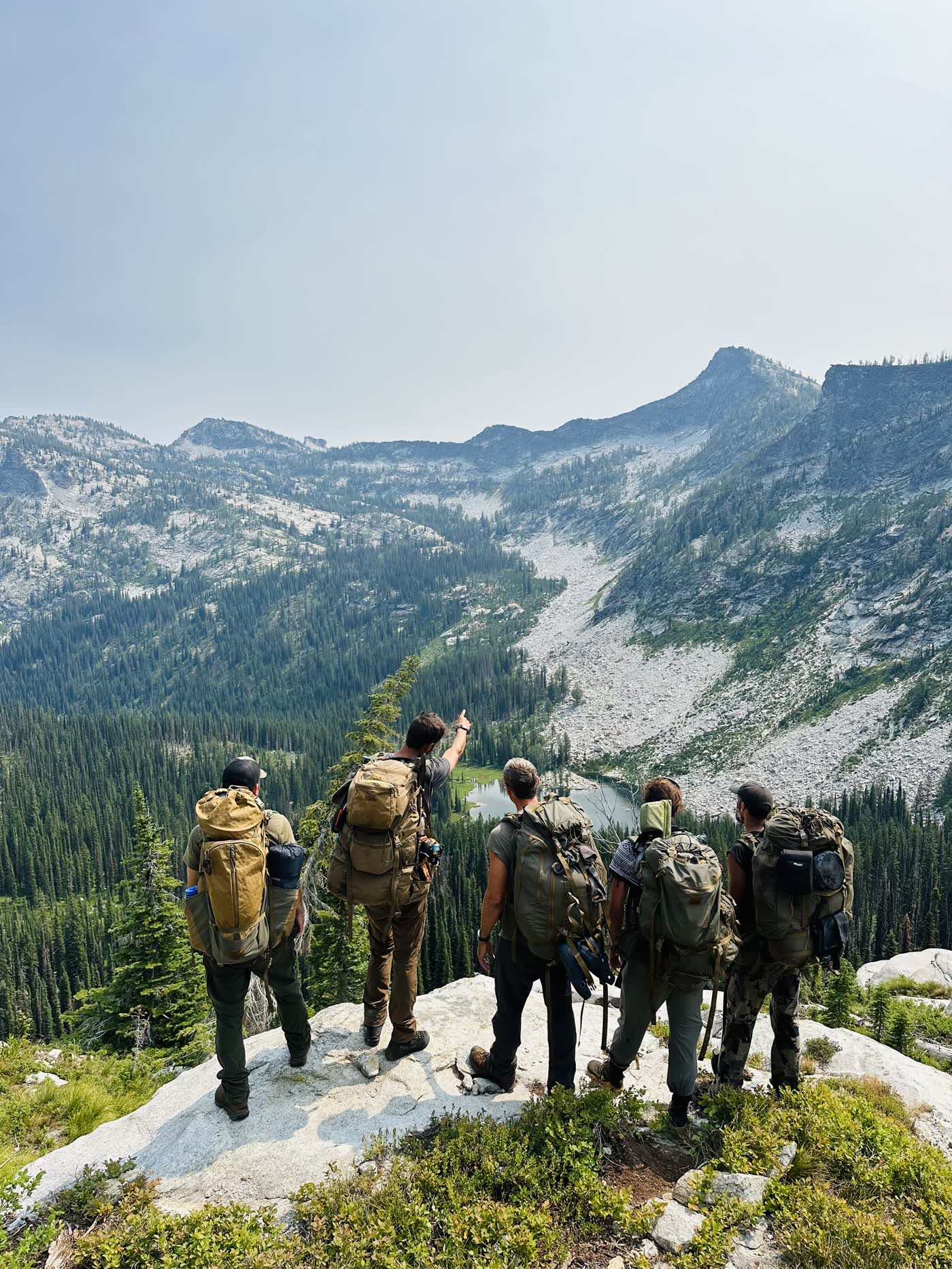 Five hikers with packs looking out over a granite basin